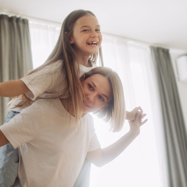 Happy mother piggybacking adorable little daughter at home.